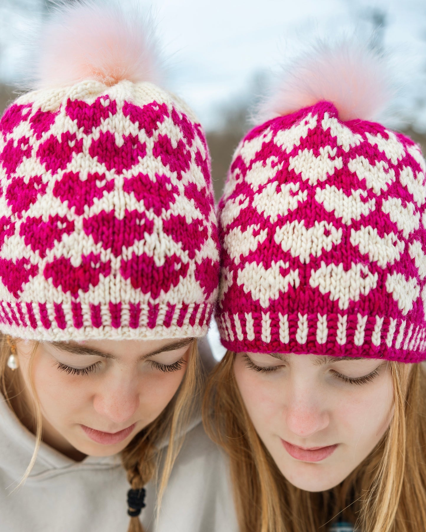 Two people wearing pink and white patterned knit hats in a snowy background