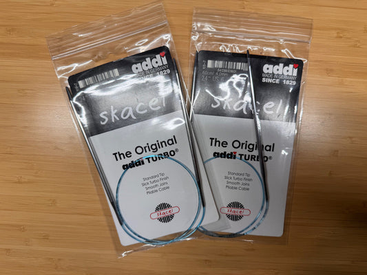 Two pairs of circular needles in packaging on a wooden surface